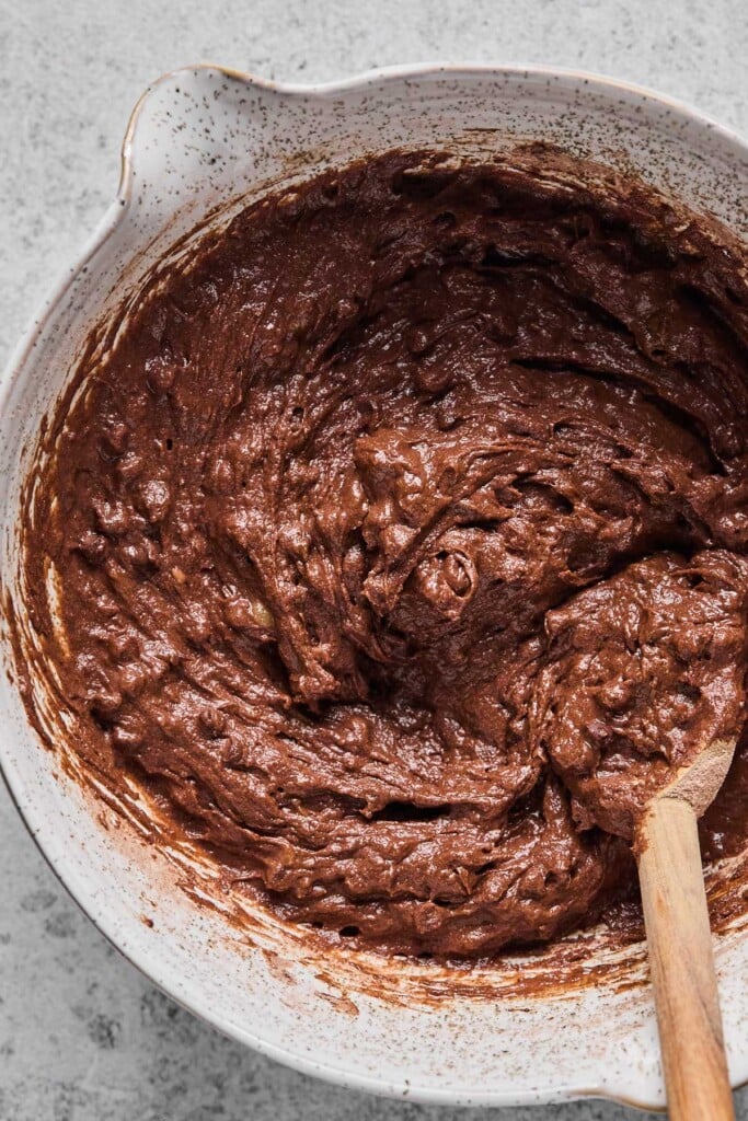 A mixing bowl with chocolate batter and a wooden spoon in it.