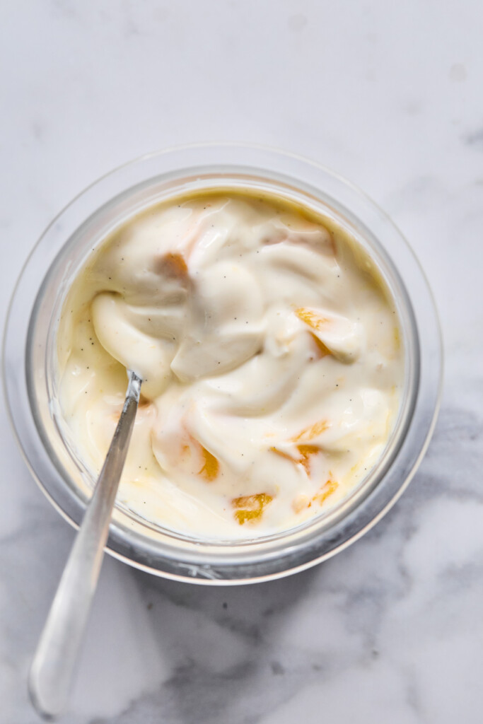 Greek yogurt mixed with honey, vanilla, and fresh diced mango in a pint container. There is a spoon in the container as well.