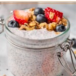 A jar of protein chia pudding topped with strawberries, blueberries, and granola. The jar is sitting on a plate.