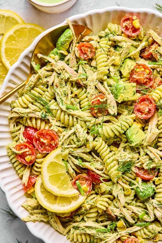 Chicken bacon ranch pasta salad in a large white bowl. It is garnished with lemon slices and fresh dill. Next to the bowl are lemon slices.