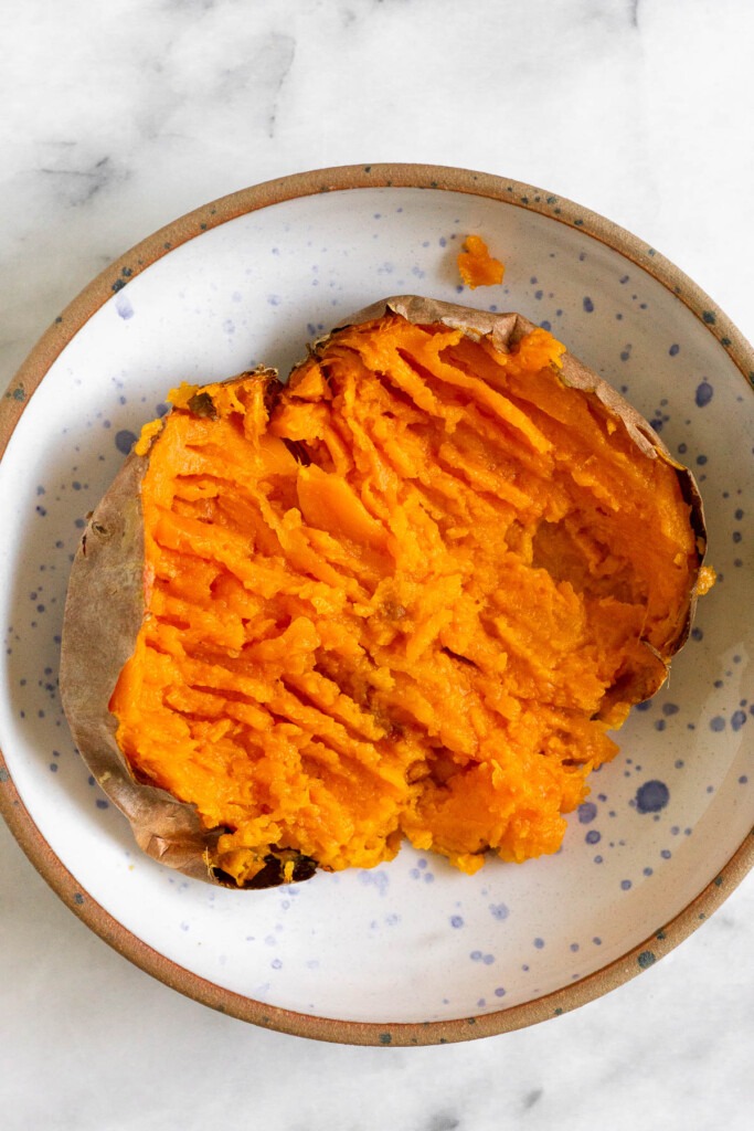 A bowl with a cook sweet potato that has been cut in half and smashed down some with a fork.