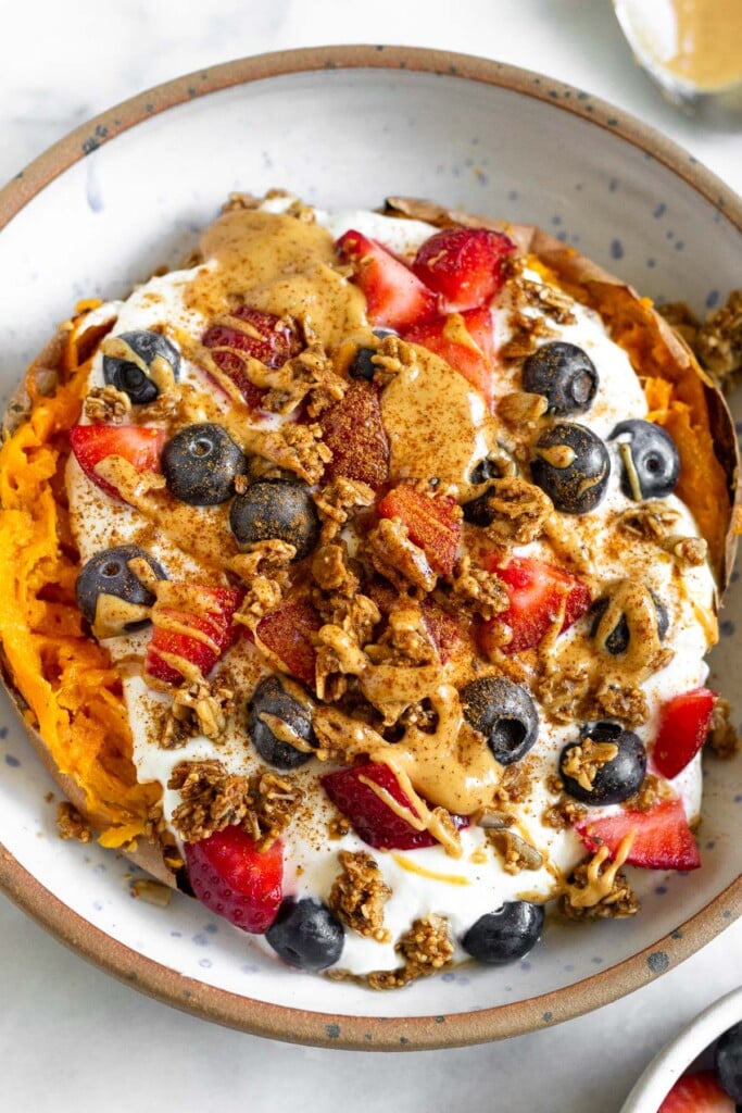 A sweet potato stuffed with greek yogurt, berries, granola, and peanut butter in a bowl. It is topped with a sprinkle of cinnamon.