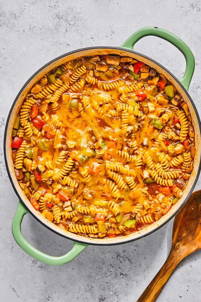Large enameled pan filled with meat and veggies in a red sauce. A wooden spoon is in the pot.