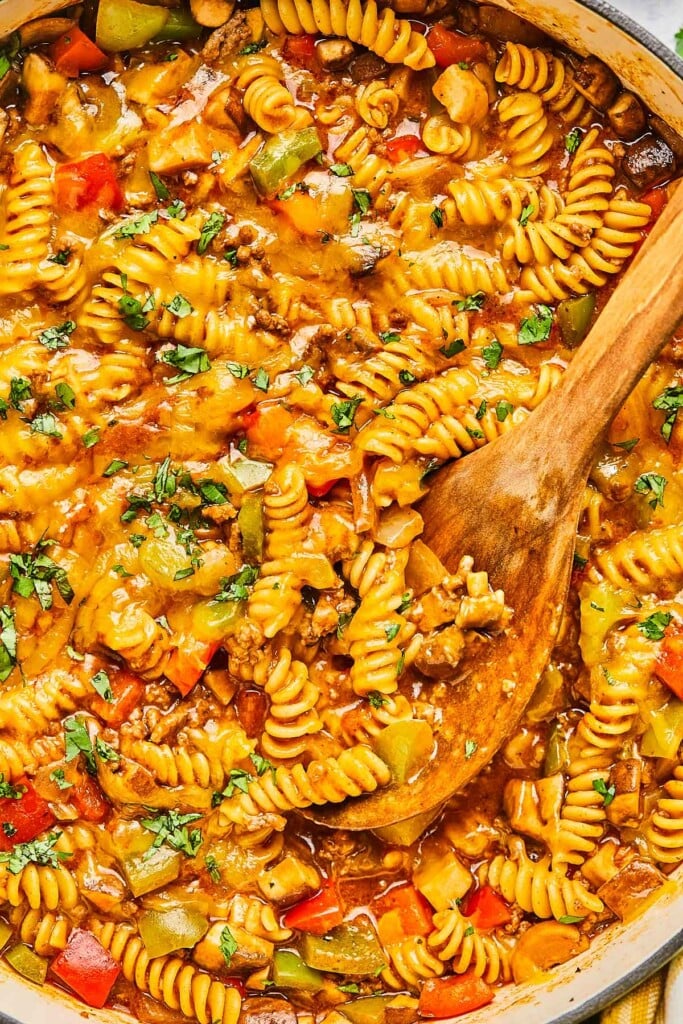 Close up of pot of beef enchilada pasta topped with melted cheese. A wooden spoon is in the pot as well.