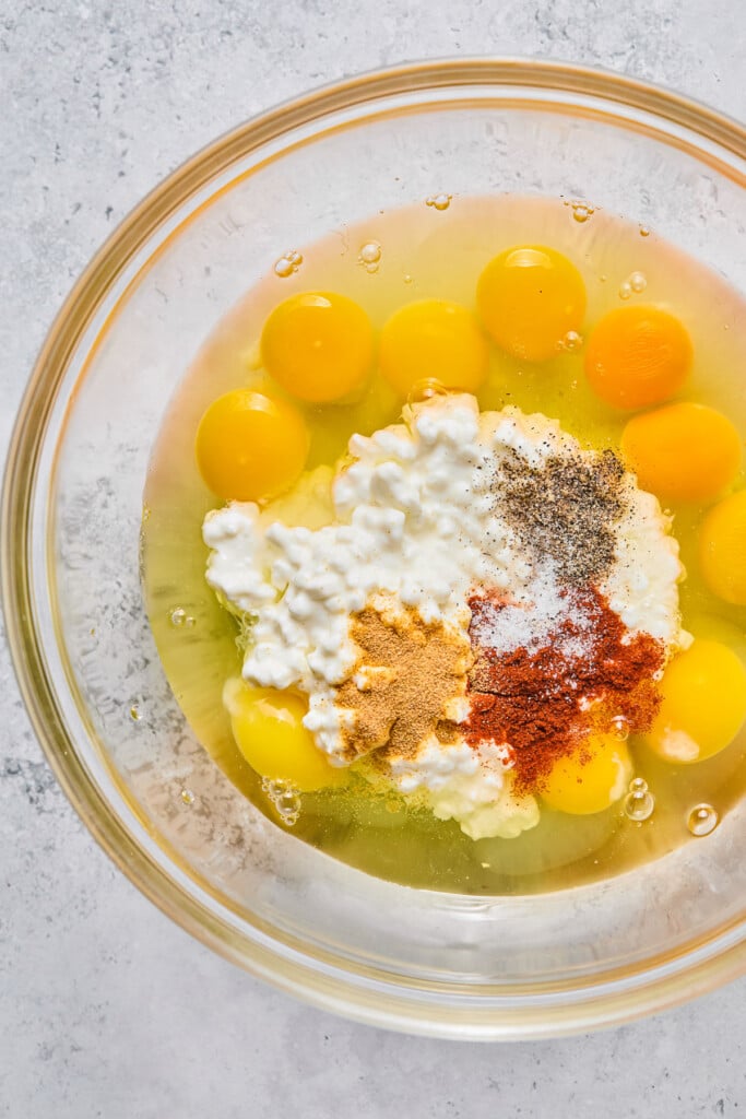 Glass bowl with raw eggs, cottage cheese, and spices before it is mixed together.