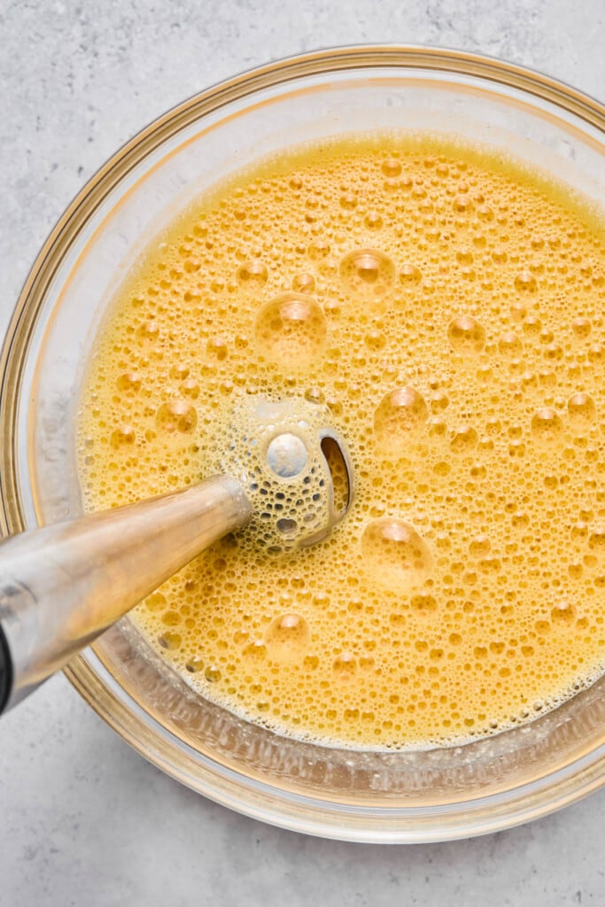 Glass bowl with a whisked egg mixture with an immersion blender in it.