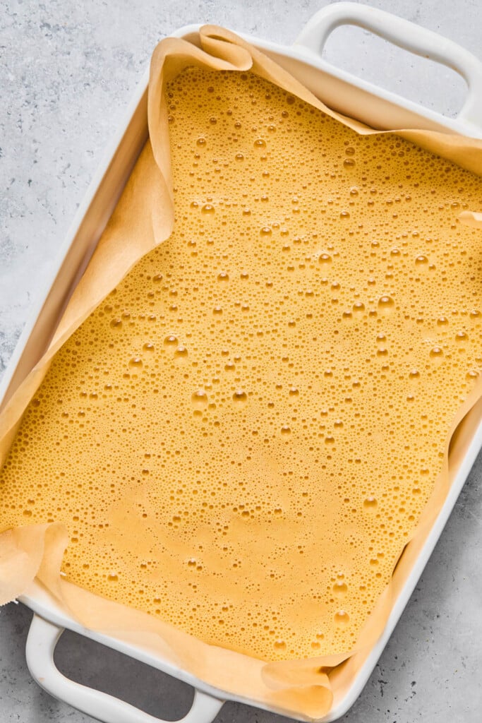 Baking dish lined with parchment paper with a whisked egg mixture in it.