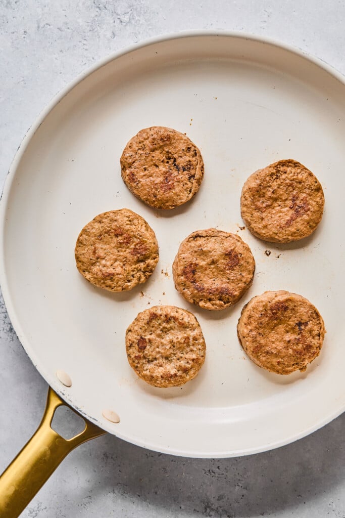 Six chicken sausage patties cooking in a large skillet.