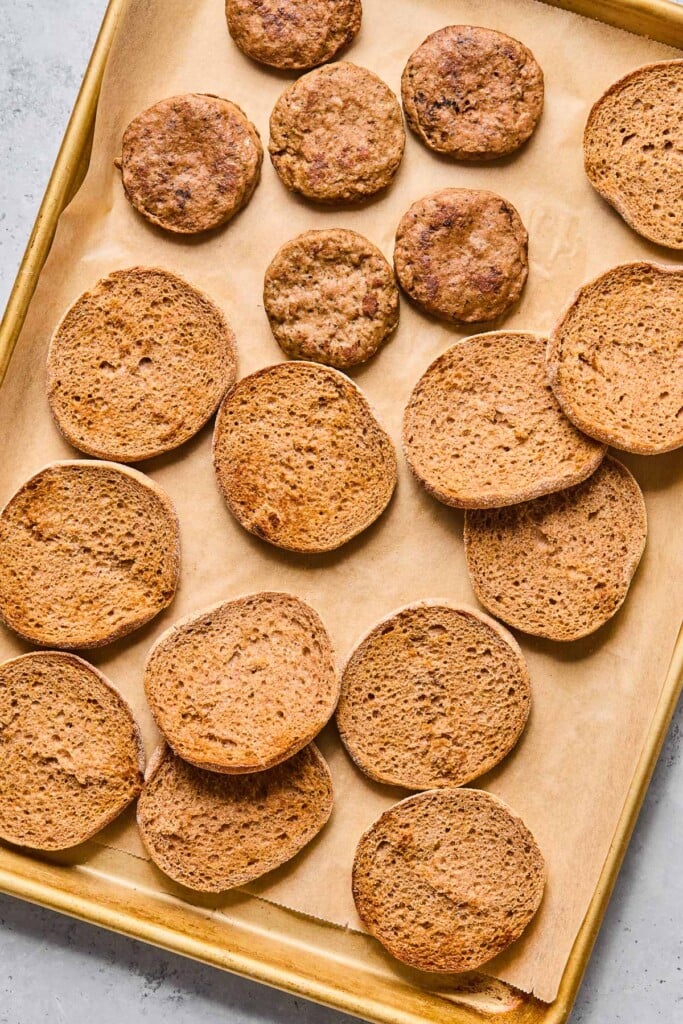 Toasted English muffins spread across a baking sheet that is lined with parchment paper.