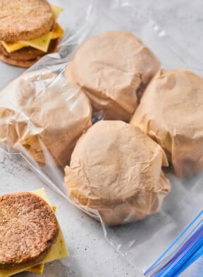 Postpartum freezer breakfast sandwiches wrapped in parchment paper in a large plastic bag. Next to the bag are two sandwiches that haven't been wrapped up yet.