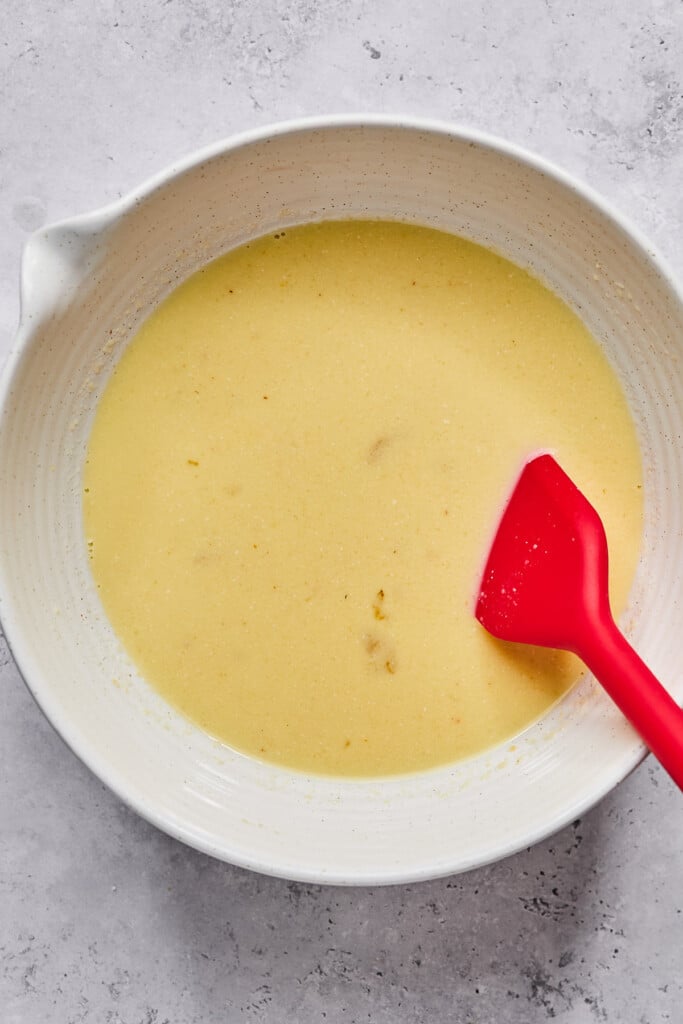 Large mixing bowl with a mixture of egg, milk, and vanilla in it. There is a red spatula in the bowl as well.