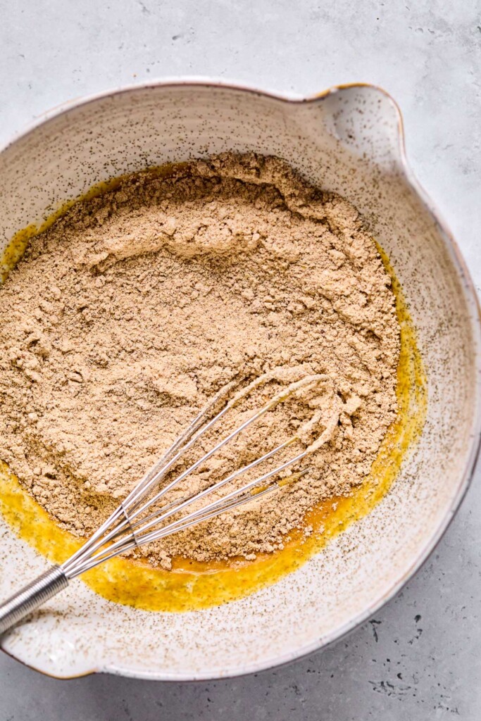 A mixing bowl with dry ingredients on top of a wet batter before it is mixed. A whisk is also in the bowl.