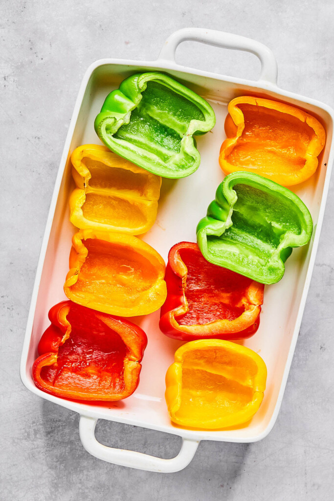 Par-baked halved bell peppers cut side up in a large white casserole dish.