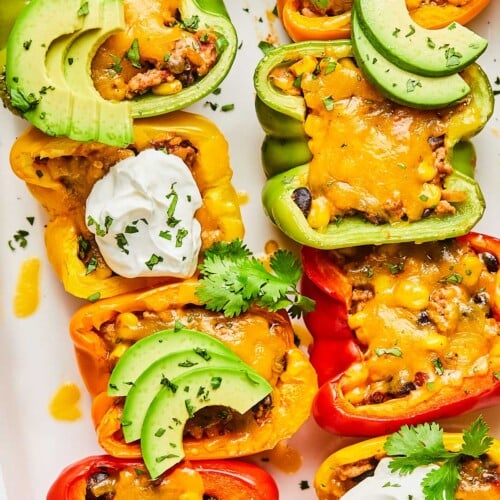 An overhead shot of taco stuffed peppers with melted cheese topped with sour cream, avocado slices, and cilantro in a white casserole dish.