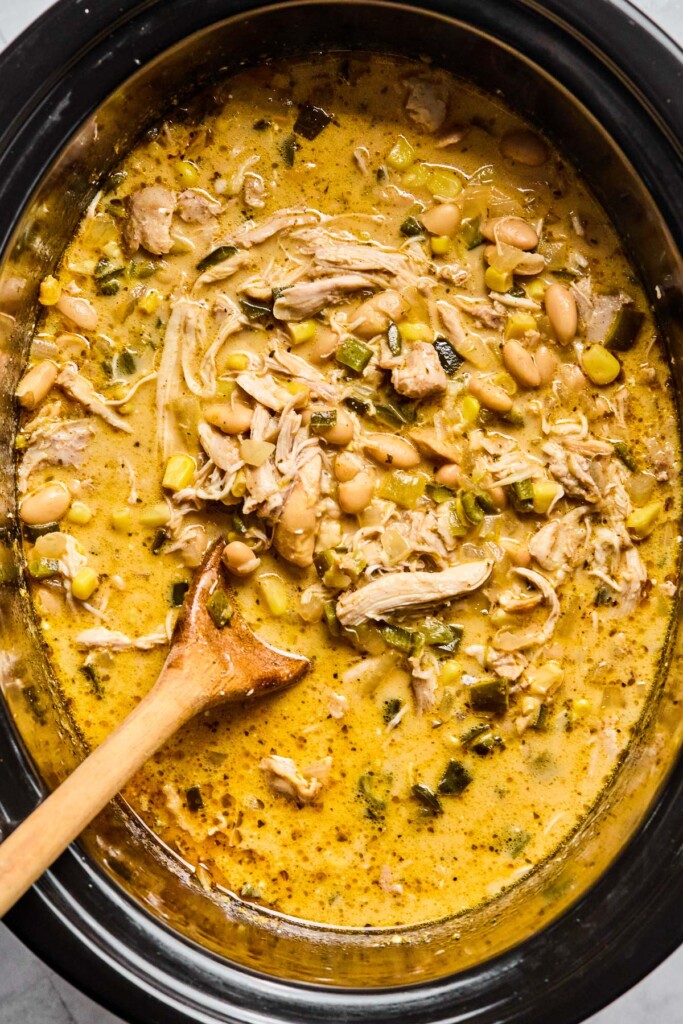 Overhead shot of white chicken chili in a crockpot with a wooden spoon in it.