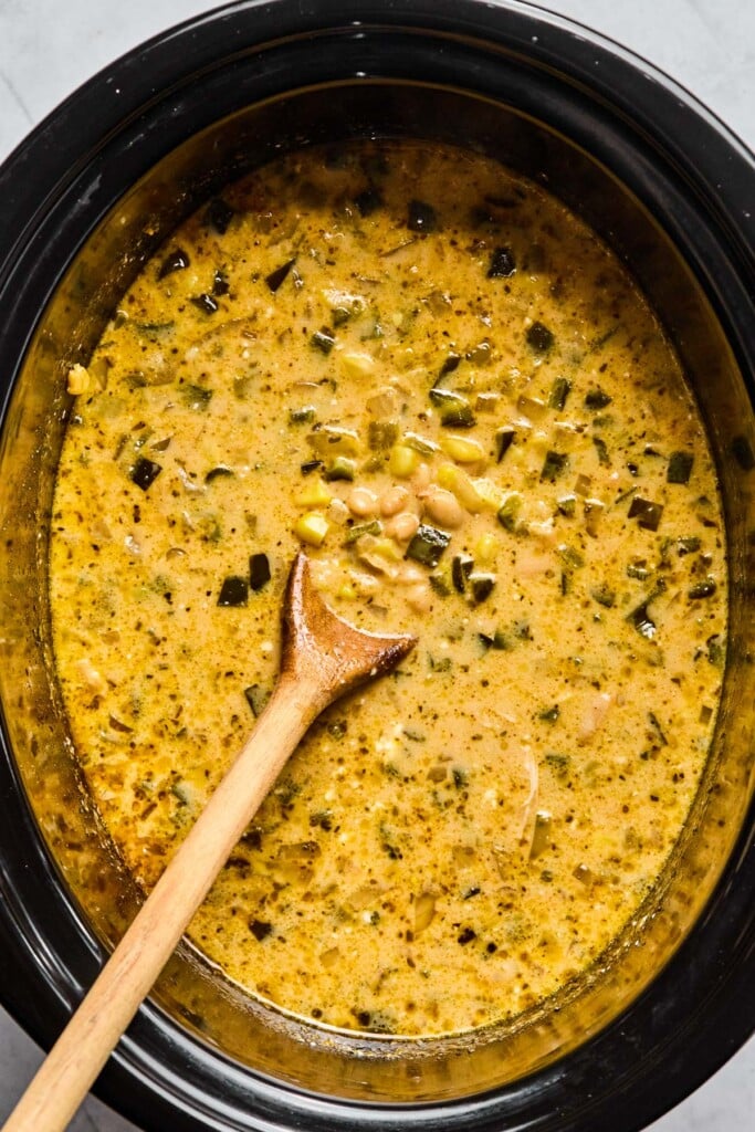 Overhead shot of a creamy soup in a slow cooker. A wooden spoon is in the slow cooker as well.