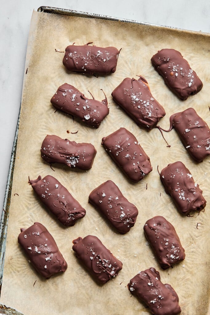 Homemade butterfinger candy bars on a baking sheet that is lined with parchment paper. They are garnished with flaky sea salt.