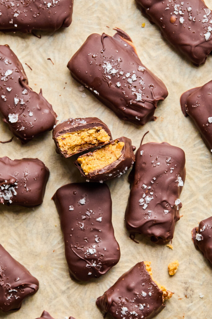 Overhead shot of homemade butterfingers on a spread apart on a piece of parchment paper. One of the bars is broken in half and standing up so you can see the inside.