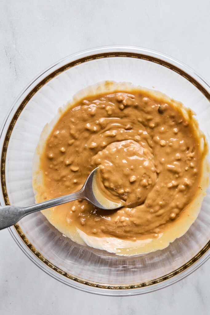 Crunchy peanut butter mixed with a little honey in a glass mixing bowl with a spoon in it.