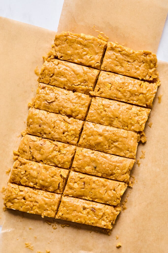 A thick peanut butter dough on parchment paper that has been cut into 14 equal-sized bars.