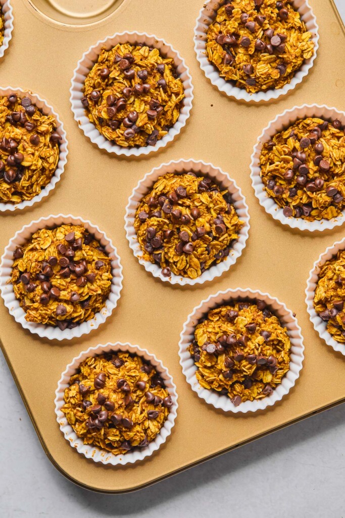 Pumpkin oatmeal chocolate chip muffins in white silicone liners in a muffin tin right after they were baked.