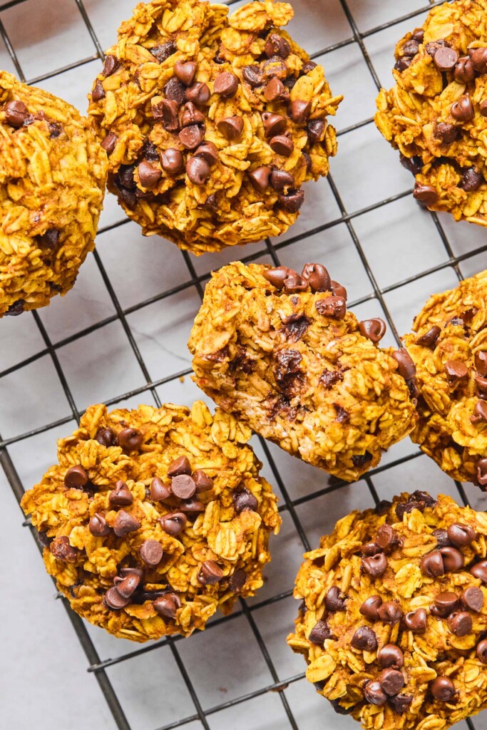 Overhead shot of healthy pumpkin oatmeal muffins spread on a metal cooling rack. The one in the middle is sitting on it's side with a bite taken out of it.