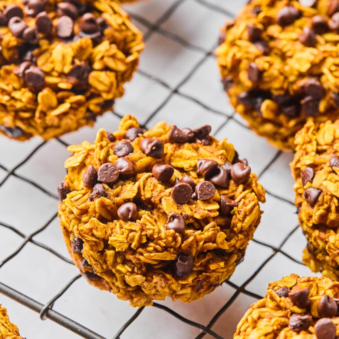 Pumpkin oatmeal muffins on a metal cooling rack. In the back off to the side is a bowl of rolled oats.