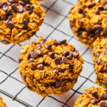 Pumpkin oatmeal muffins on a metal cooling rack. In the back off to the side is a bowl of rolled oats.