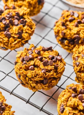 Pumpkin oatmeal muffins on a metal cooling rack. In the back off to the side is a bowl of rolled oats.