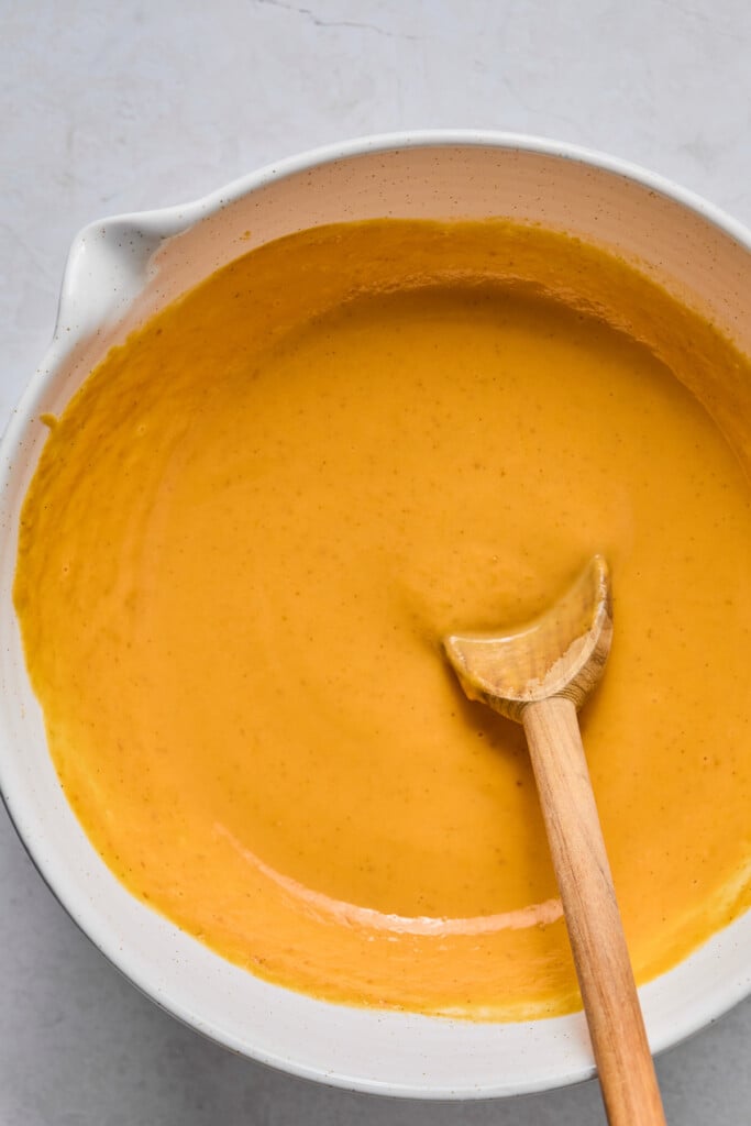 White mixing bowl filled with a wet batter with a wooden spoon in it.