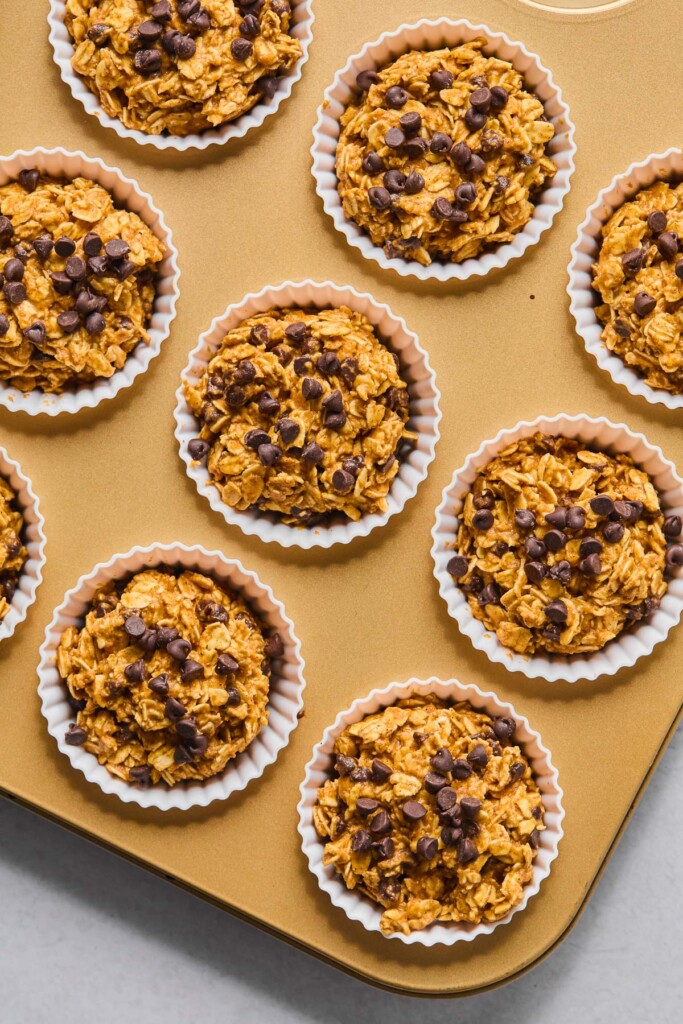 Muffin tin filled with white liners with chocolate oatmeal banana muffins in them before they are baked.