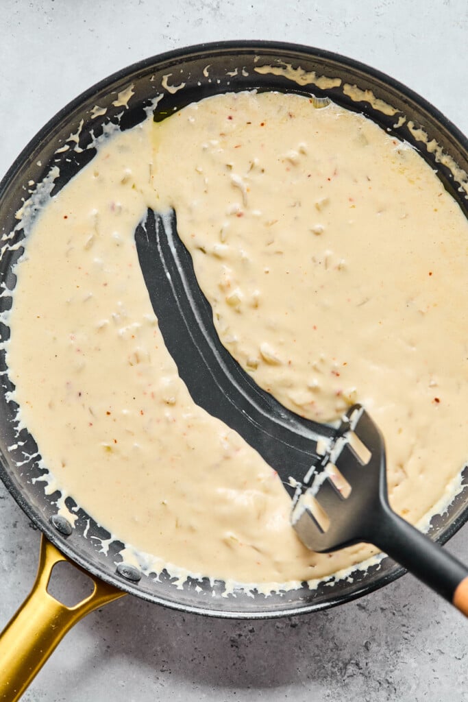 Skillet of a creamy white sauce with a spatula running through it.