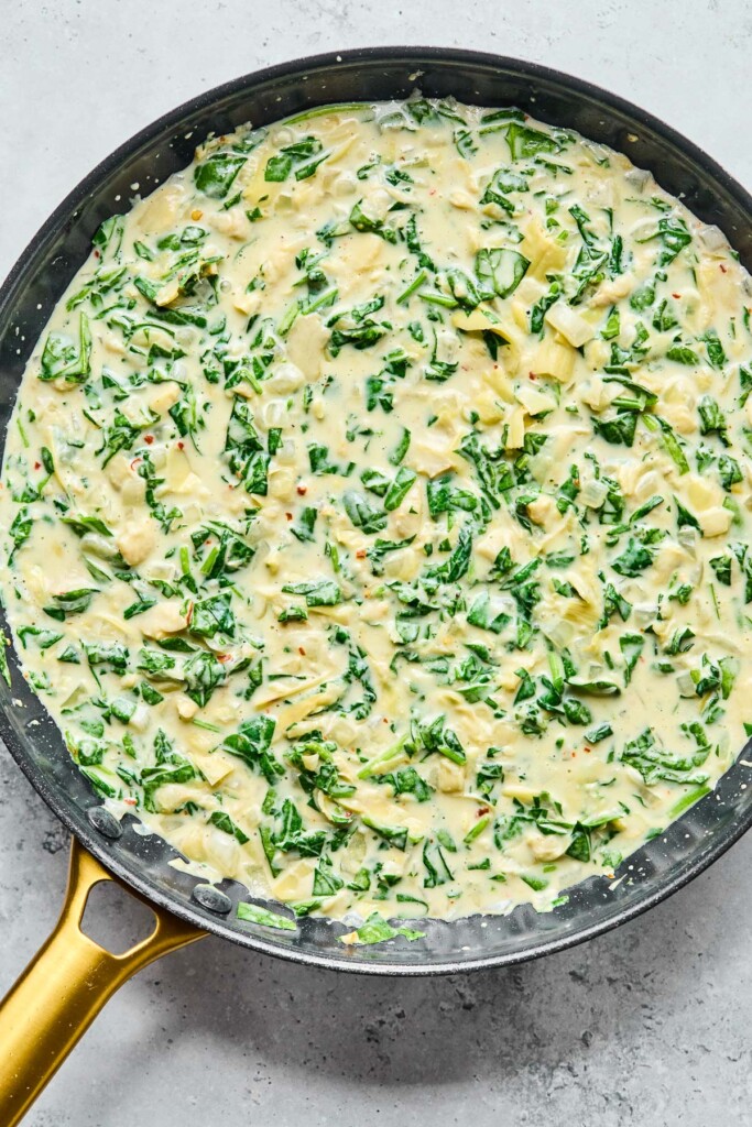 Overhead shot of a skillet with a creamy spinach and artichoke sauce in it.