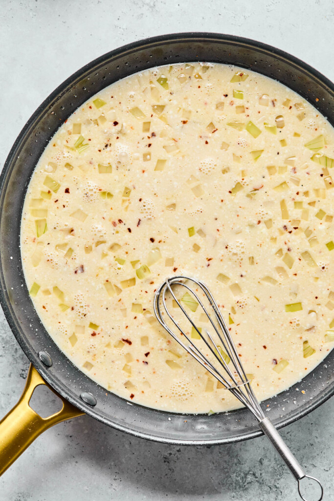 A creamy white sauce in a skillet with a whisk in it.