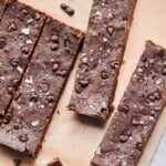 Chocolate protein bars spread out on a piece of parchment paper with mini chocolate chips around them.