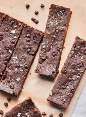 Chocolate protein bars spread out on a piece of parchment paper with mini chocolate chips around them.