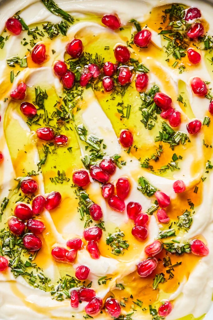Close up of whipped ricotta with honey, olive oil, rosemary, and pomegranates seeds on top of it.