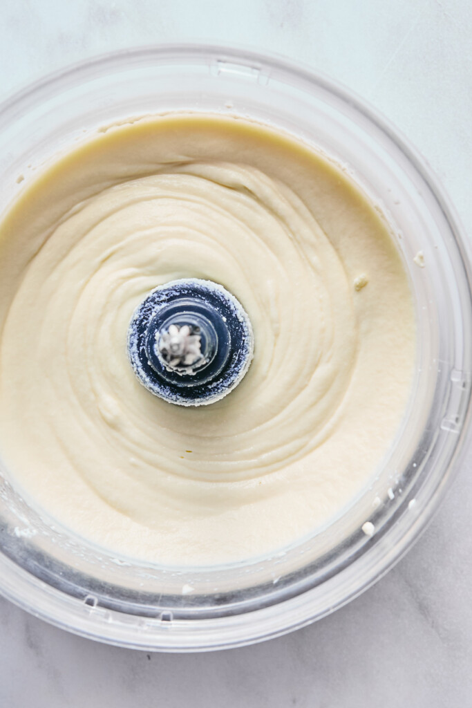 Overhead shot of whipped ricotta cheese in the bowl of a food processor.
