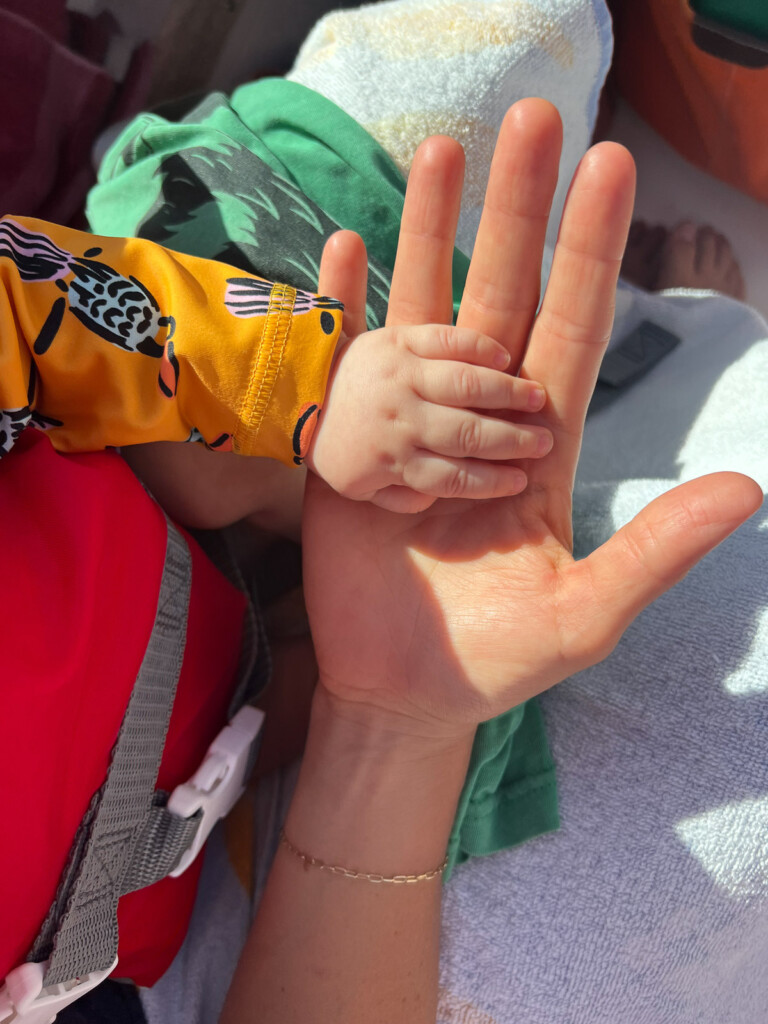 A mom holding her hand open with her baby's hand on top of it. You can just see their hands and arms.