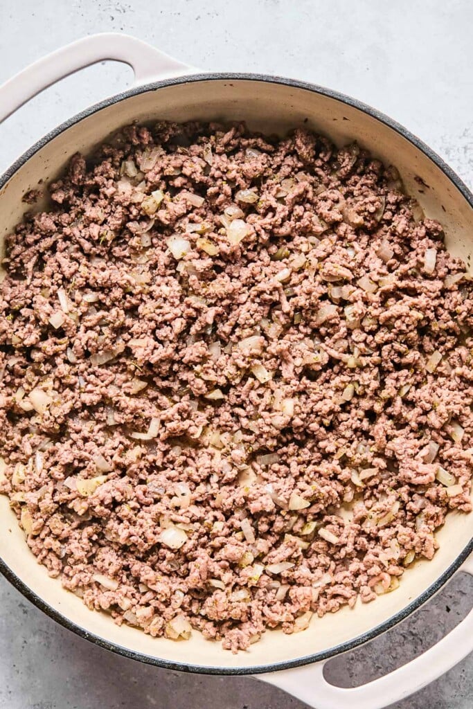 Overhead shot of a enameled pan filled with sautéed onions and ground beef.