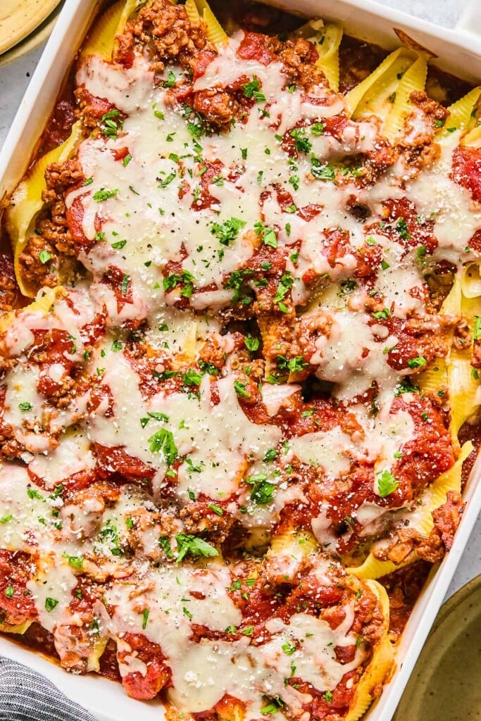 Overhead shot of beef stuffed shells in a large baking dish. They are topped with melted cheese, fresh chopped parsley, and grated parmesan cheese.