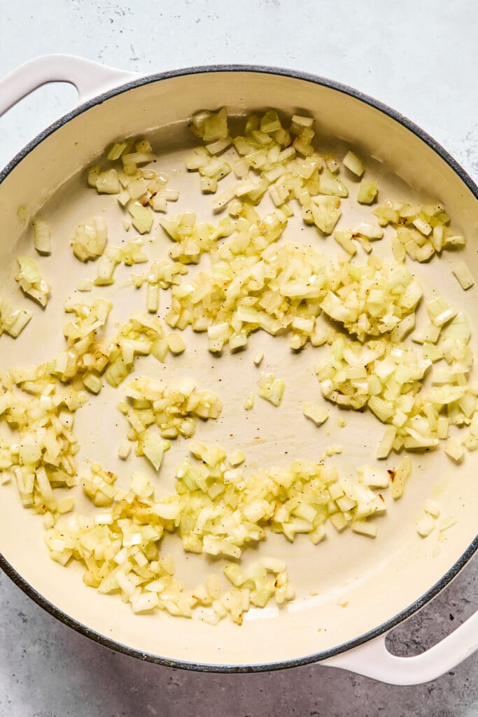 Overhead shot of a enameled pan filled with sautéed onions and garlic.