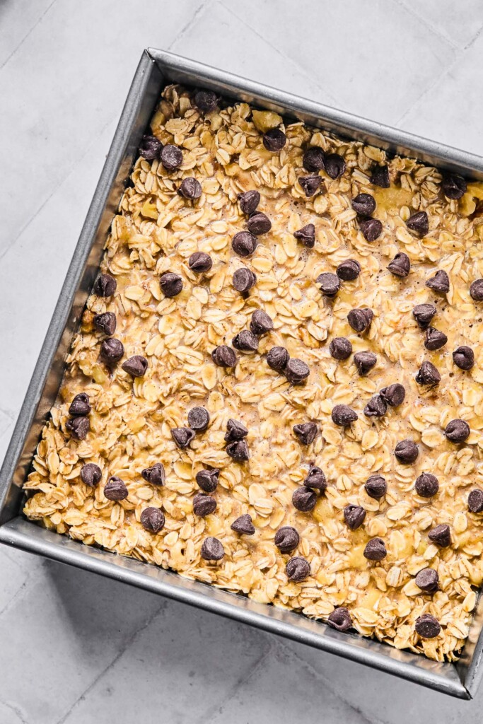 A large baking dish filled with an oatmeal mixture topped with chocolate chips before it is baked.