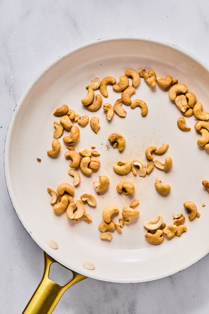Small white skillet with toasted cashews in it.