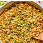 Healthy egg roll in a bowl in a large white skillet. It is garnished with black sesame seeds, sliced green onions, and cilantro and a wooden spoon is in the pan as well.