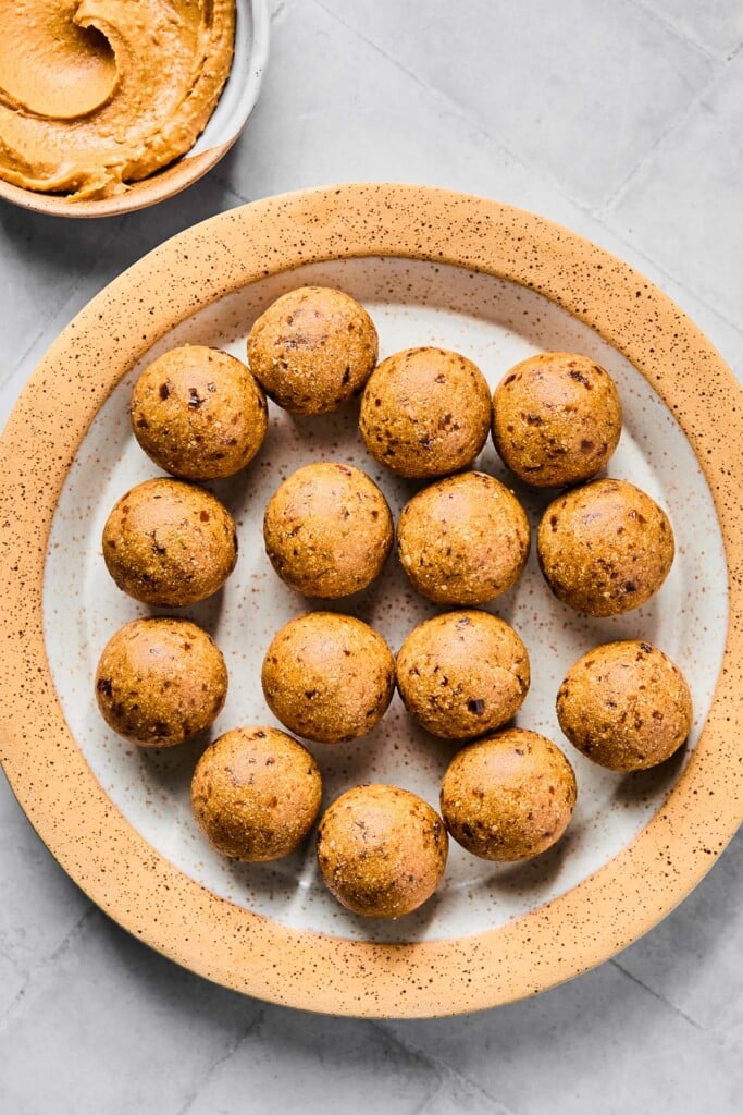 Overhead shot of no bake peanut butter protein balls on a white and brown plate. Next to the plate is a bowl of peanut butter.