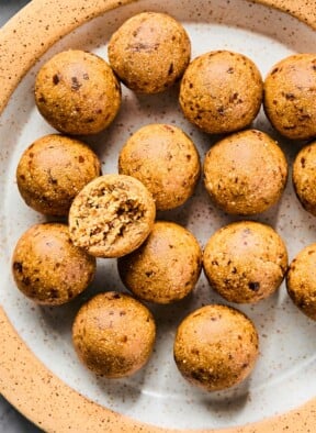 A plate of peanut butter protein balls. One of the balls is on top of the rest and it has a bite taken out of it.