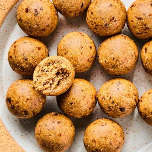 A plate of peanut butter protein balls. One of the balls is on top of the rest and it has a bite taken out of it.