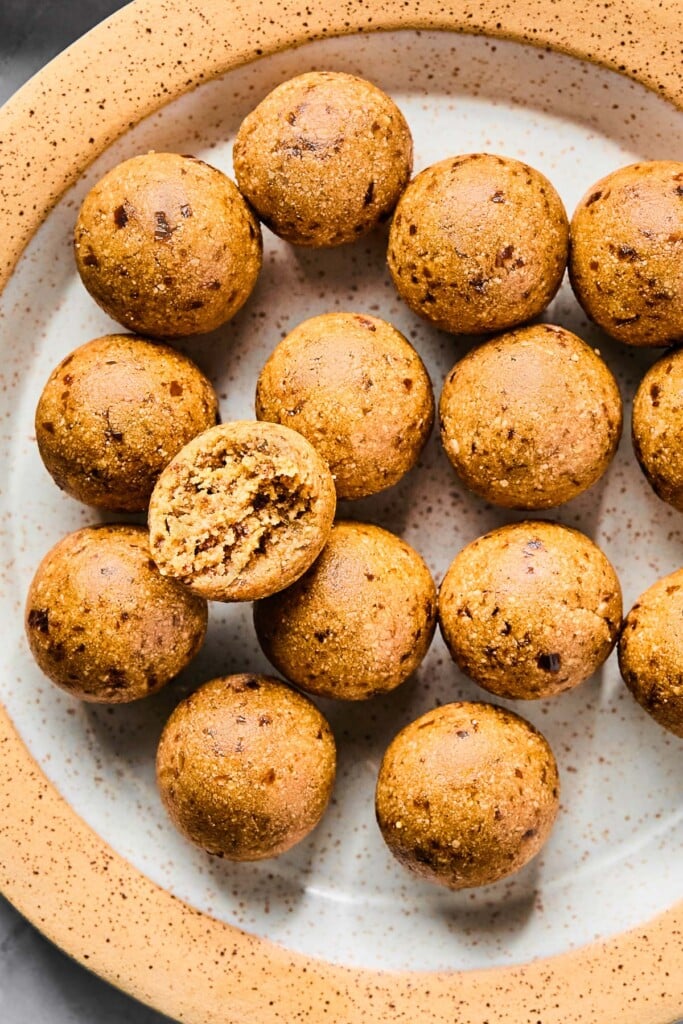 A plate of peanut butter protein balls. One of the balls is on top of the rest and it has a bite taken out of it.