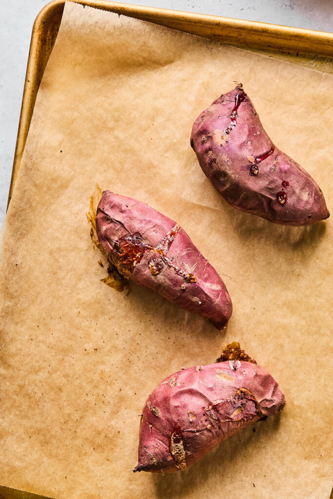 Three baked sweet potatoes on a baking sheet lined with parchment paper.